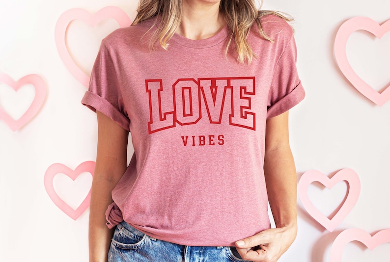May include: A pink t-shirt with the text "LOVE VIBES" in red block letters.