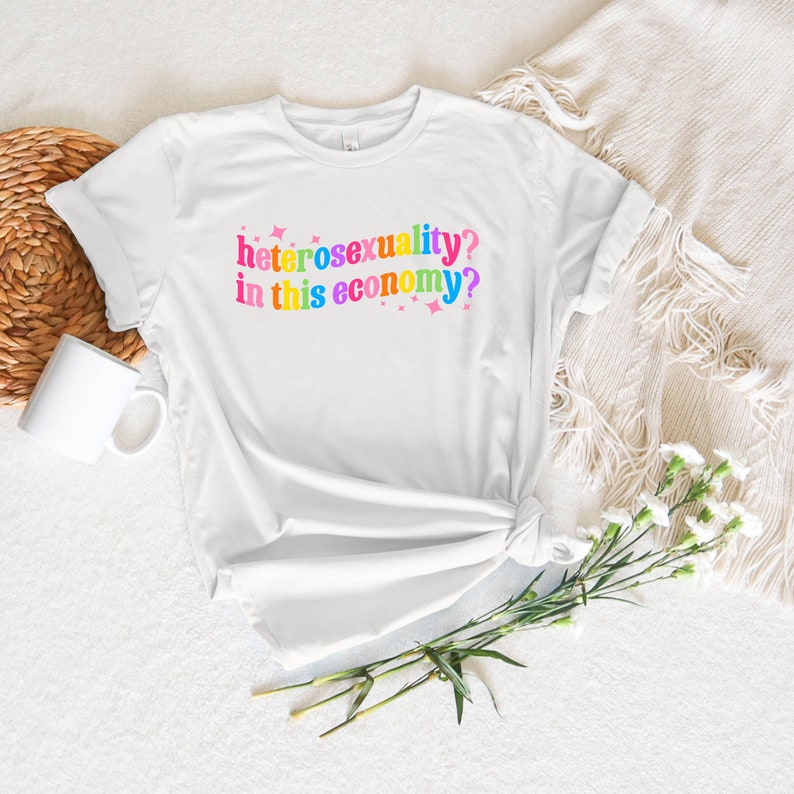 May include: White t-shirt with the text "heterosexuality? in this economy?" printed in rainbow colors.