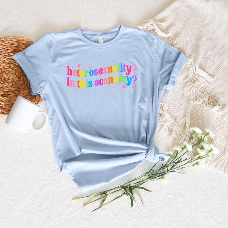 May include: Light blue t-shirt with the text "heterosexuality? in this economy?" in rainbow colors.