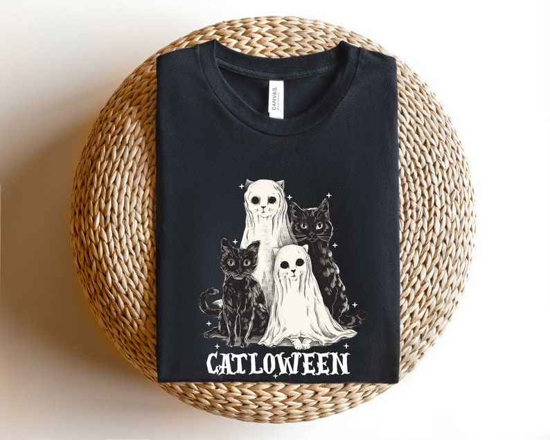 K&ouml;nnte beinhalten: Schwarzes T-Shirt mit einem Aufdruck von drei Katzen, die als Geister verkleidet sind. Der Text "Catlowteen" ist unter den Katzen aufgedruckt.