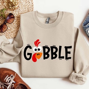 May include: A beige sweatshirt with a black and orange turkey graphic and the text "GOBBLE".