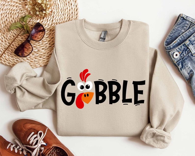 May include: A beige sweatshirt with a black and orange turkey graphic and the text "GOBBLE".