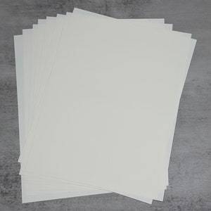 Może przedstawiać: Stos białych arkuszy papieru, prawdopodobnie do drukowania lub rękodzieła.