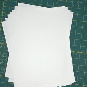 May include: A stack of white paper sheets on a green cutting mat.