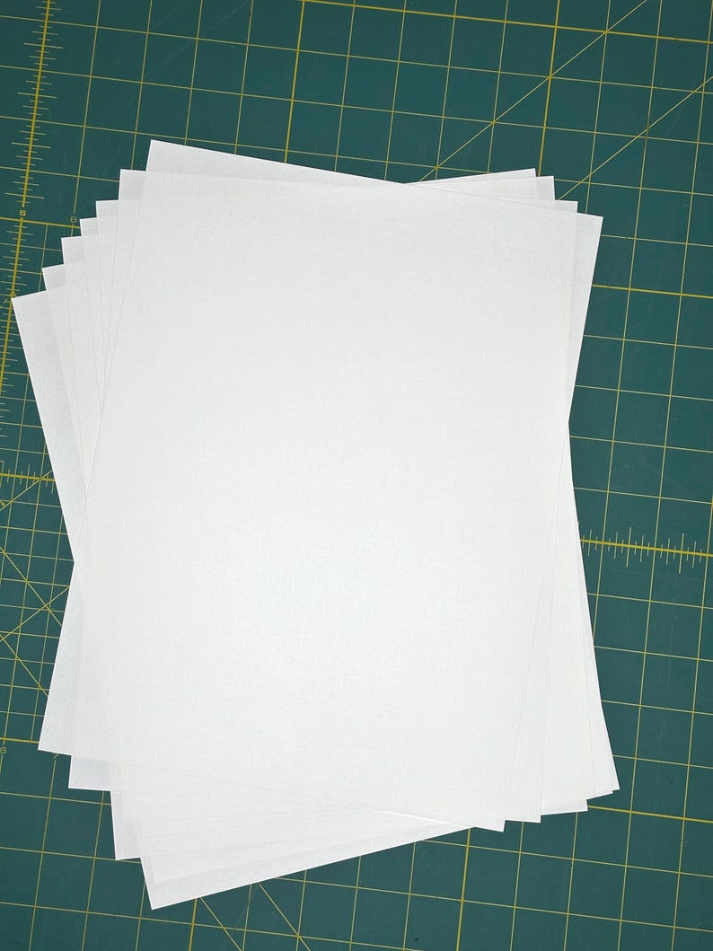 May include: A stack of white paper sheets on a green cutting mat.