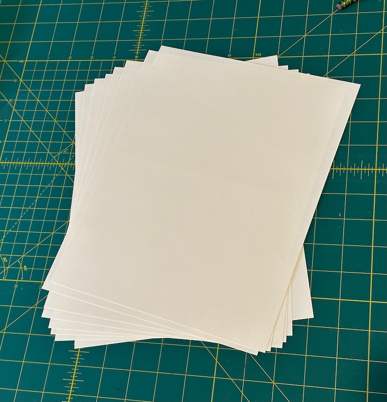 Może przedstawiać: Stos białego papieru do scrapbookingu na zielonej macie do cięcia.