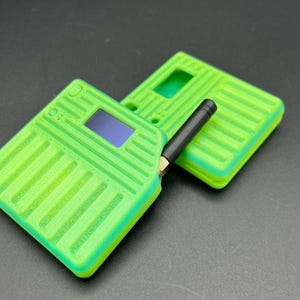 May include: Two lime green electronic devices with a rectangular shape and a ridged design. One device has a small screen and a black antenna. The other device is placed behind it. The background is a dark gray color.