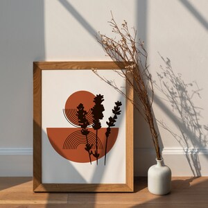 May include: A framed print with a minimalist design featuring a stylized silhouette of a plant with brown and orange geometric shapes. The print is in a wooden frame and is hanging on a white wall.