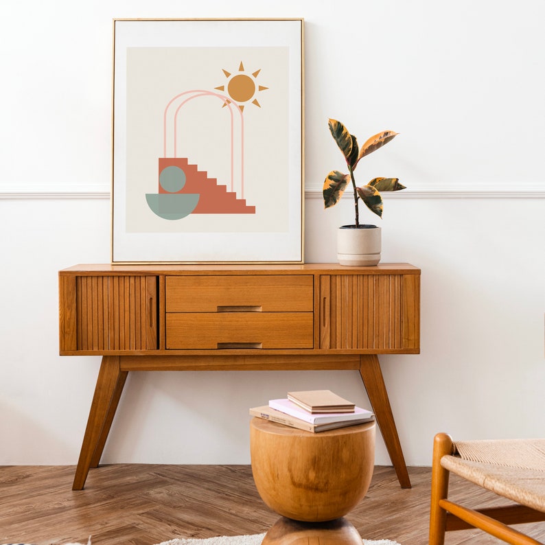 May include: A mid-century modern wooden console table with two drawers and a geometric abstract art print above it. A potted plant sits on the table and a wooden stool with books on top sits in front of the table.