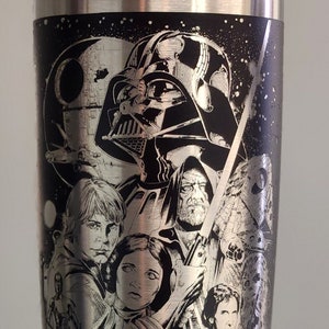 May include: A stainless steel tumbler featuring a black and white etched design of characters from Star Wars. The design includes Darth Vader, Luke Skywalker, Princess Leia, Han Solo, Chewbacca, and R2-D2.