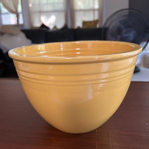 May include: A bright yellow ceramic mixing bowl with a smooth, glossy finish. The bowl features a wide, rounded rim and three distinct horizontal ridges encircling the upper exterior, providing a textured detail to the otherwise simple, deep basin.