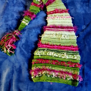 May include: A green and pink crocheted hat with a long, pointed top. The hat has a fuzzy texture and is decorated with stripes of different colors.