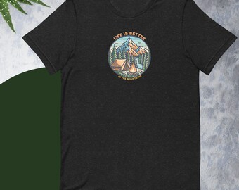 May include: Dark gray t-shirt with a circular graphic featuring a mountain scene. The design includes a cabin, campfire, and text that reads "LIFE IS BETTER IN THE MOUNTAINS". The shirt is made of a soft material.