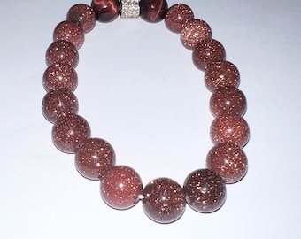 May include: A brown beaded bracelet with a silver clasp and a single red bead with gold flecks.