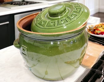 May include: A green ceramic crock with a lid. The lid has a decorative pattern of a Greek key design. The crock is glazed and has a shiny finish.