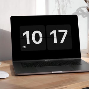May include: A black laptop displaying the time 10:17 PM on its screen. A white mouse sits to the left of the laptop on a wooden desk. A vase with dried flowers and an incense stick are also on the desk.