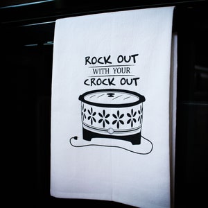 Peut inclure: Une serviette de cuisine blanche avec du texte noir qui dit "Rock out with your crock out". Une illustration en noir et blanc d'une mijoteuse se trouve sous le texte.