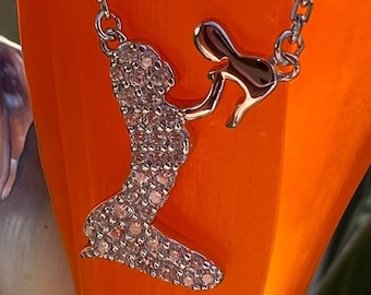 May include: Silver necklace with a pendant of two figures holding hands. The figures are made of silver and have a sparkly finish.