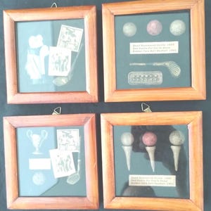 May include: Four framed golf memorabilia displays. Each wooden frame contains a dark background with golf balls, tees, and vintage images. The frames are square and have a natural wood finish. Text is visible in the frames.