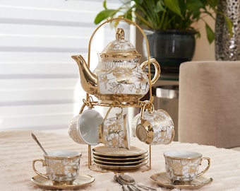 Könnte beinhalten: Ein Teeservice aus weißem Porzellan mit goldenen Blumenmustern, bestehend aus einer Teekanne mit Deckel, mehreren Tassen und Untertassen. Das Set ist auf einem goldfarbenen Metallständer angeordnet, ergänzt durch weitere Tassen, Untertassen und Löffel.