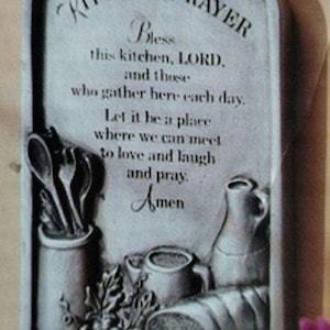 May include: A gray, rectangular kitchen plaque with the words "Kitchen Prayer" and a prayer. The plaque features embossed images of kitchen utensils, bread, grapes, and a pitcher. A small heart is at the top.