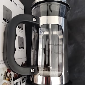 May include: Stainless steel French press coffee maker with a black handle and base. The clear glass carafe has measurements in ounces and milliliters. The product is labeled as 12oz/350ml.