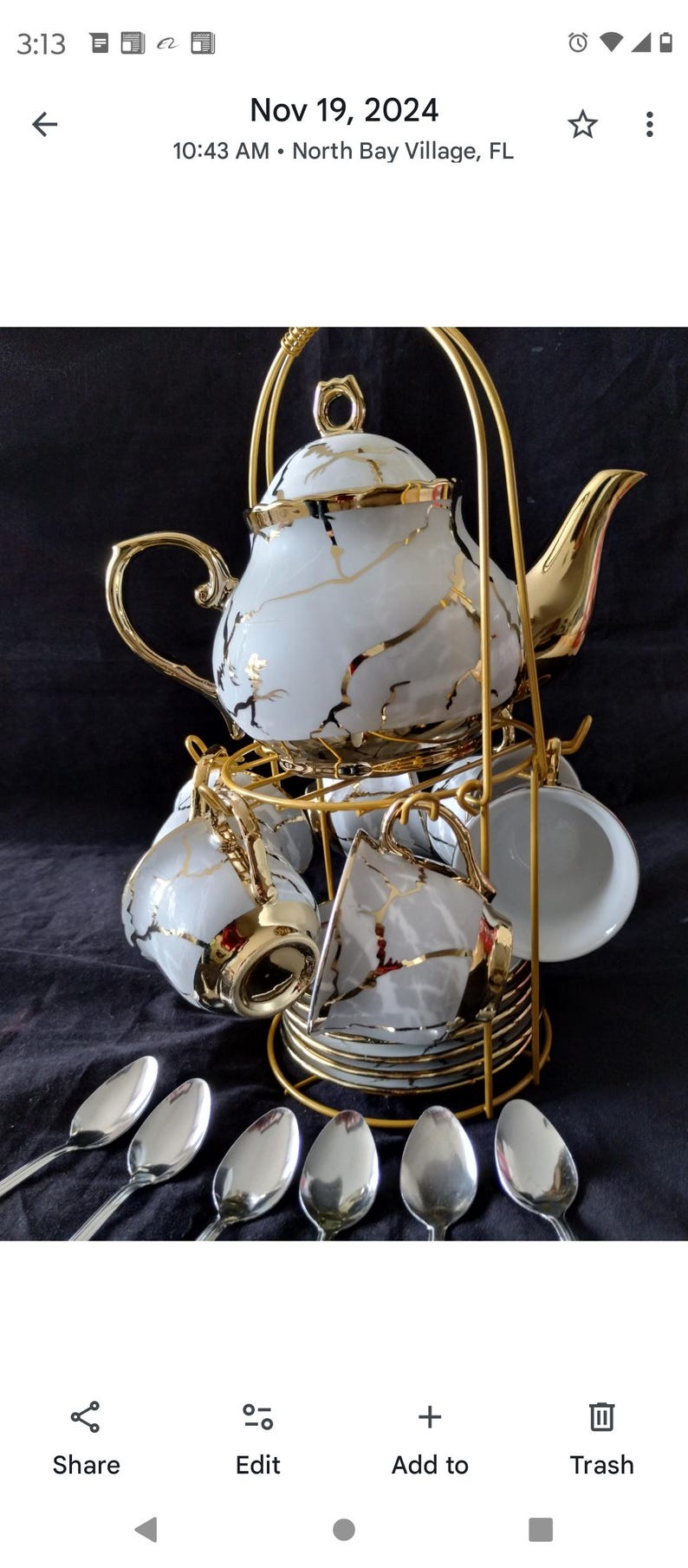 May include: A white porcelain tea set with gold accents, including a teapot, cups, saucers, and spoons. The set is displayed on a gold metal stand. The teapot and cups have a gold vein design.