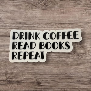 以下が含まれることがあります： 「DRINK COFFEE READ BOOKS REPEAT」と書かれた黒い文字の白いステッカー。ステッカーは角が丸い長方形で、木目模様の木製の表面に貼られています。