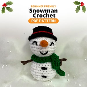 Peut inclure: Un bonhomme de neige crocheté avec un chapeau noir, un nez orange et une écharpe verte. Le bonhomme de neige a un visage souriant et des bras en forme de bâton. Le texte "BEGINNER FRIENDLY Snowman Crochet PDF PATTERN" est inclus.