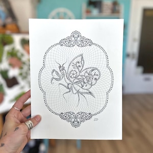 May include: A black and white line drawing of a praying mantis with butterfly wings inside a decorative frame. The drawing is on white paper and has a delicate, intricate design.
