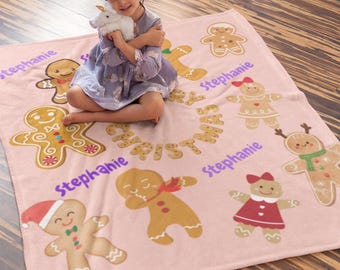 May include: Pink fleece blanket with a gingerbread man theme. The blanket features multiple gingerbread men in various poses, including a gingerbread man doing the dab. The blanket is personalized with the name "Stephanie" repeated throughout.
