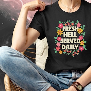 May include: A black t-shirt with a floral design and the text "Fresh Hell Served Daily".