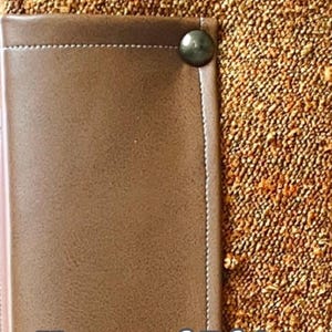 May include: Close-up of a brown leather detail with a decorative metal stud on a textured, speckled fabric. The text "Hemmed Edges For A Finished Look" is visible.