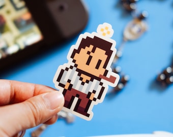 May include: A pixelated sticker of a cartoon character wearing a blue and white striped shirt, brown pants, and a brown hat. The character is holding a pipe in their mouth and has a small yellow star above their head.
