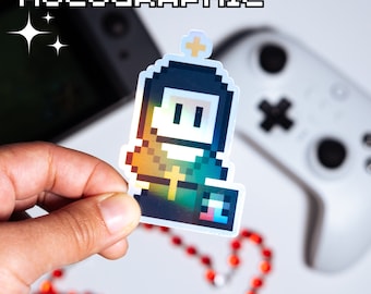 May include: A holographic sticker featuring a pixelated character wearing a green and yellow robe with a cross on the chest. The character has a black head with white eyes and a white halo. The sticker is on a white background.