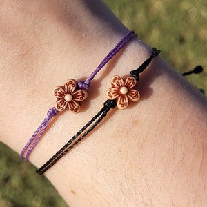 May include: Two bracelets with brown flower charms. One bracelet is purple and the other is black.