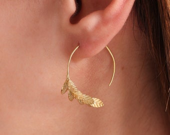 Puede incluir: Pendientes de aro dorados con un delicado diseño de hojas. Los pendientes están hechos de un alambre fino y tienen una forma curva.