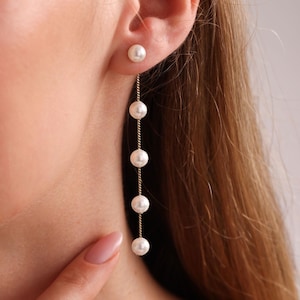 May include: A pair of gold earrings with a single pearl at the top and a chain of pearls dangling down.