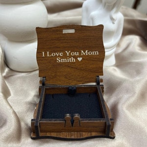 May include: A wooden box with a hinged lid. The lid is open and has the inscription "I Love You Mom Smith" with a heart symbol. The box is lined with black velvet.