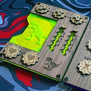 May include: Two wooden game trackers with laser-cut details. One has a neon green interior with a dinosaur, the other has a blue interior. Both have rotating dials for HP, casts, and poison.