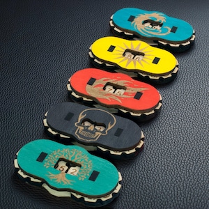 May include: Five colourful wooden game tokens with various designs: a dragon, sun, flames, skull, and tree. Each token has a number display. The tokens are painted in blue, yellow, red, black, and teal, with a natural wood border.