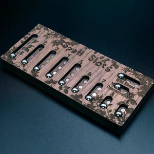 Könnte beinhalten: Ein rechteckiger Zauberplatz-Tracker aus Holz mit eingravierten Blumenmustern und dem Text Spell Slots, Wild Shape und Concentration. Er verfügt über vertikale Schlitze mit kleinen silbernen Metallkugeln zur Verfolgung von Spielstatistiken.