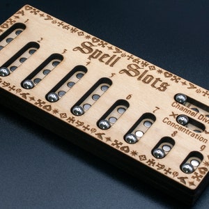 May include: A wooden spell slots tracker with nine slots, each with a small metal ball. The tracker has the words "Spell Slots" engraved on it, along with the numbers 1 through 9. The tracker also has the words "Channel Divinity" and "Concentration" engraved on it.