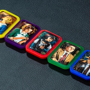 Puede incluir: Una colección de cinco imanes rectangulares y coloridos. Cada imán presenta una ilustración vintage diferente de personas. Los imanes tienen marcos amarillos, morados, rojos, verdes y azules. Las imágenes están sobre un fondo oscuro y texturizado.