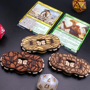 Könnte beinhalten: Drei Holzzählmarken mit unterschiedlichen Designs und Zahlen. Die Marken werden verwendet, um Lebenspunkte oder andere Spielstatistiken in Brettspielen zu verfolgen. Die Zahlen auf den Marken sind 44, 29 und 38.