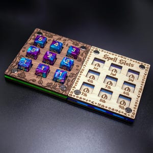 Op de afbeelding: Een houten spell slot tracker met negen slots voor dobbelstenen. De tracker heeft een blauwe en groene rand. De dobbelstenen zijn paars en blauw met gouden nummers.