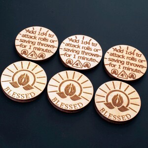 May include: Six circular wooden tokens featuring engraved designs. Three tokens display the text "Add 1d4 to attack rolls or saving throws for 1 minute" with a small triangle icon. Three tokens feature an engraved image of praying hands and the word "BLESSED".