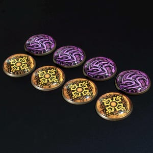 May include: A collection of seven circular cabochons arranged in two rows. Four cabochons feature a purple swirling graphic design, while three cabochons display a yellow and brown geometric pattern. Each piece has a smooth, domed surface.