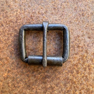 May include: A black metal buckle with a rectangular shape and a smooth, matte finish. The buckle has a single, centered, horizontal bar that slides through the loop.