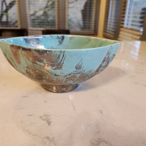 May include: A teal ceramic bowl with a marbled design in shades of brown and gold. The bowl has a wide, rounded base.